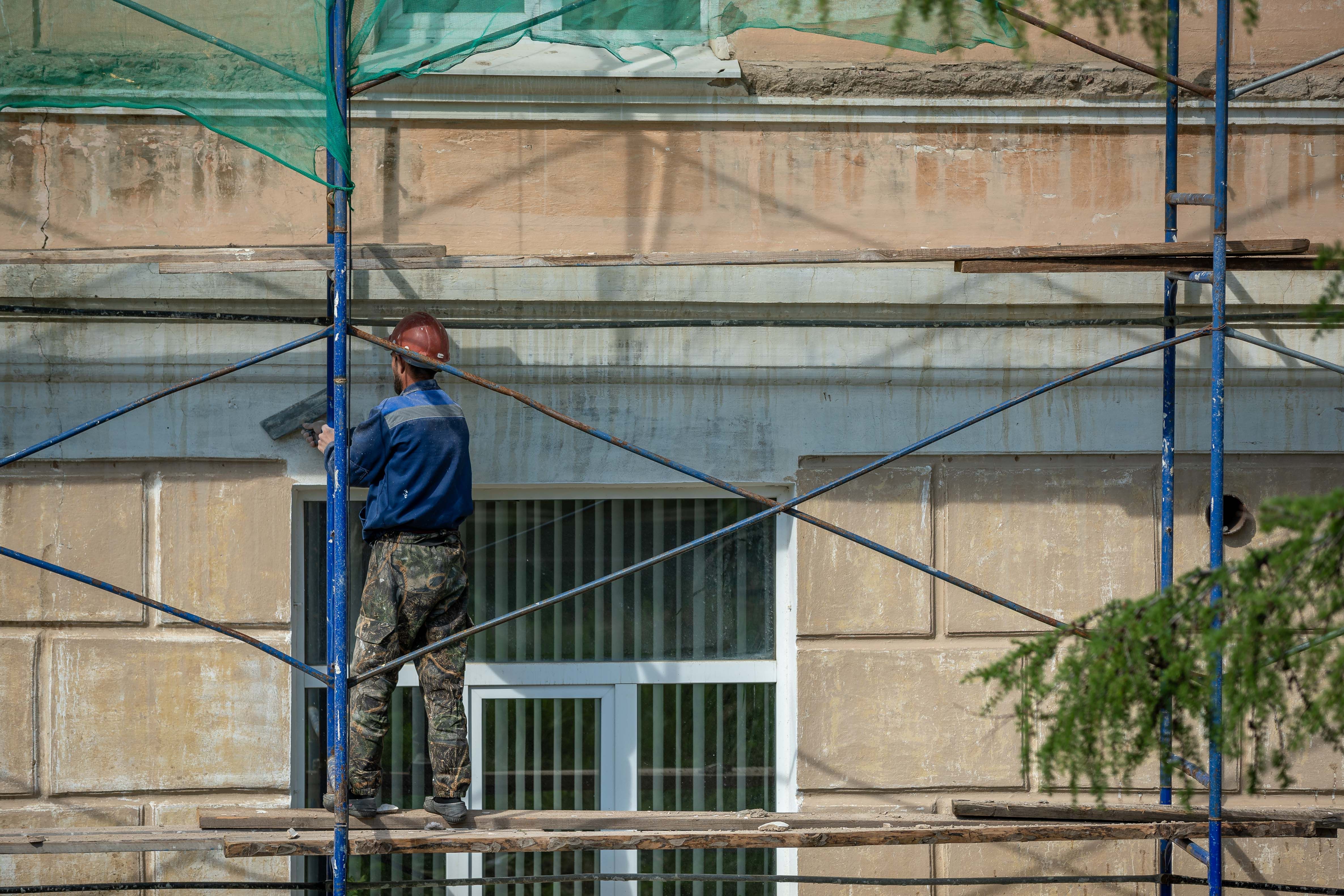 Майстер ремонтує мінеральний фасад будинку з риштування перед фінішним оздобленням